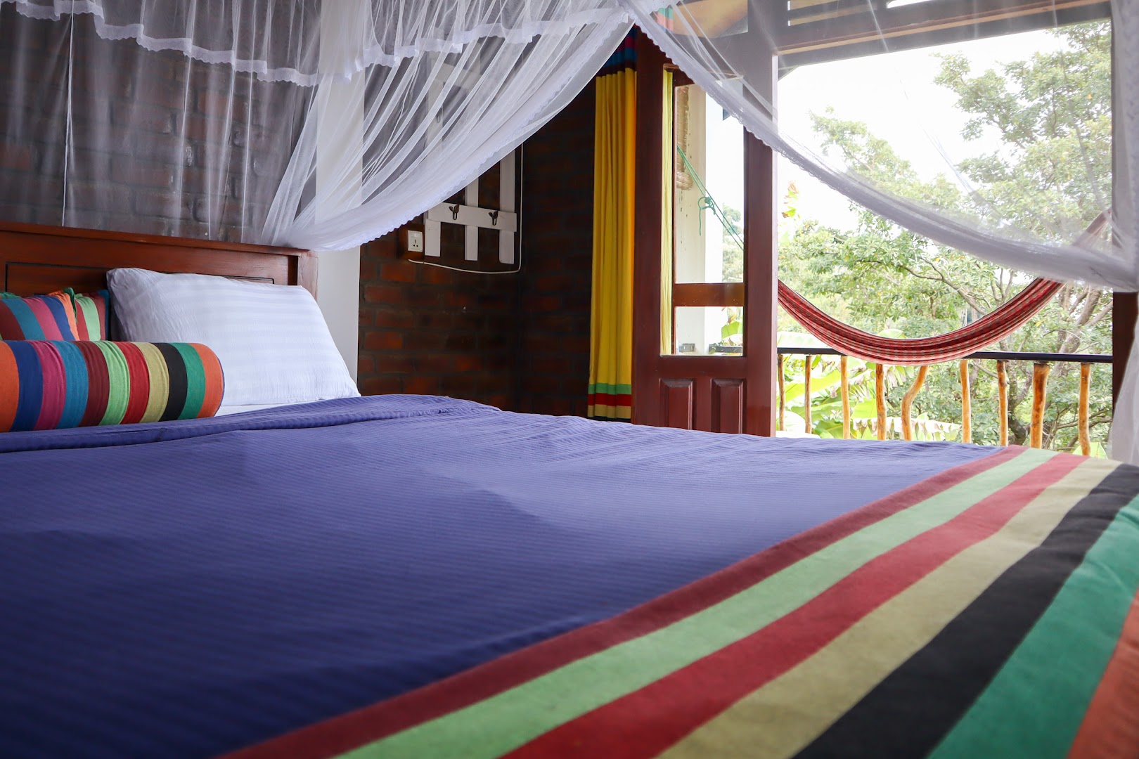 Bedroom with a white mosquito net, striped textiles, and a hammock outside